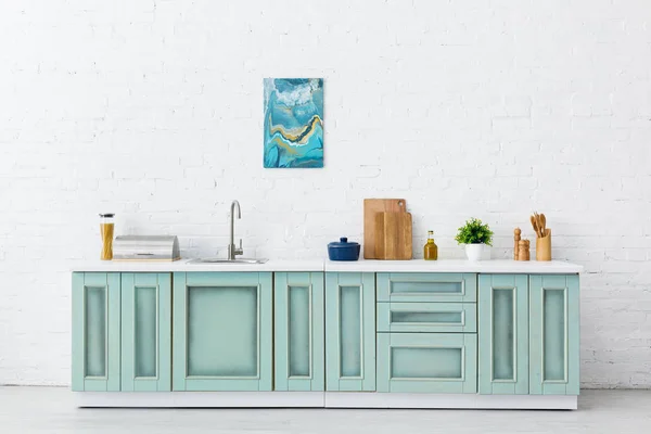 Intérieur de cuisine blanc et turquoise avec ustensiles de cuisine et peinture abstraite sur mur de briques — Photo de stock