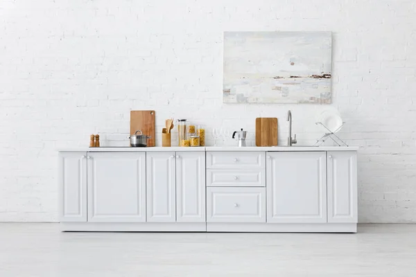 Intérieur de cuisine blanche minimaliste avec ustensiles de cuisine et peinture sur mur de briques — Photo de stock