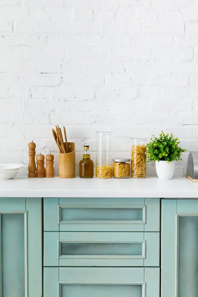 Intérieur moderne de cuisine blanche et turquoise avec ustensiles de cuisine, récipients pour aliments et plantes près du mur de briques — Photo de stock