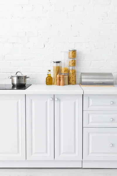 Intérieur minimaliste de cuisine blanche moderne avec plaque de cuisson à induction, nourriture, boîte à pain près du mur de briques — Photo de stock