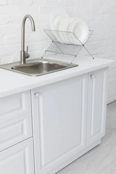 Intérieur moderne minimaliste de cuisine blanche avec évier et assiettes sur pied près du mur de briques — Photo de stock