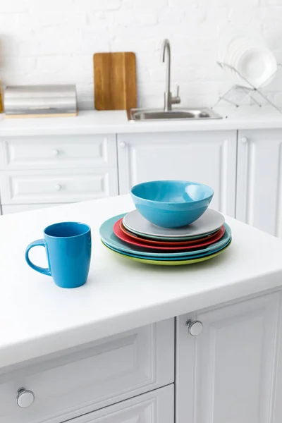Selective focus of colorful plates and cup with kitchenware near brick wall on background — Stock Photo