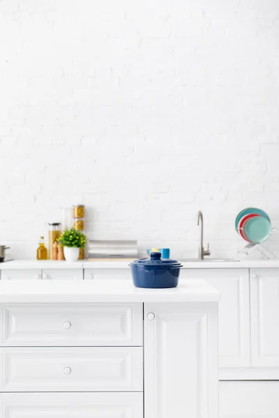 Foco seletivo de panela azul e interior da cozinha branca moderna minimalista com utensílios de cozinha e comida perto da parede de tijolo no fundo — Fotografia de Stock