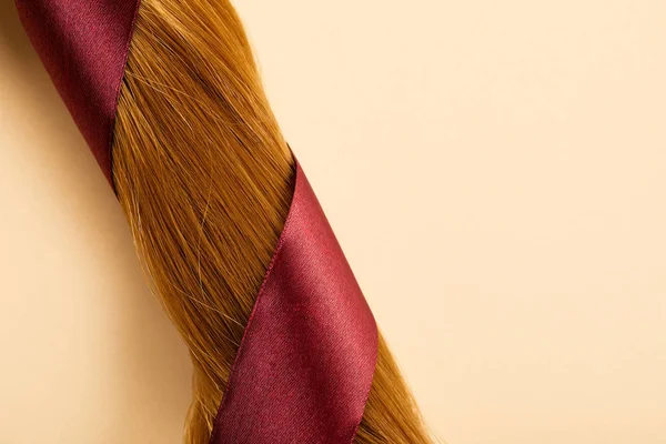 Top view of burgundy ribbon on brown hair on beige background — Stock Photo