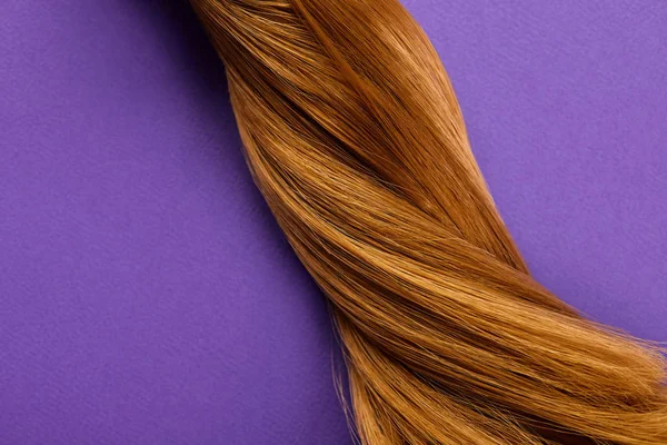 Vista superior de cabello castaño retorcido sobre fondo púrpura - foto de stock