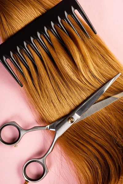 Vista dall'alto di forbici e pettine su capelli castani su sfondo rosa — Foto stock