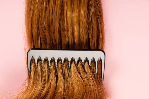 Top view of comb in brown hair on pink background — Stock Photo