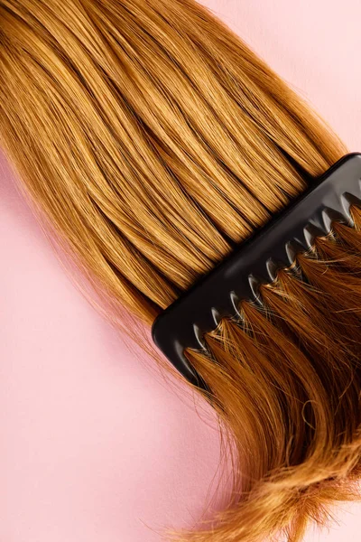 Вид сверху на коричневые волосы и расческу на розовом фоне — стоковое фото