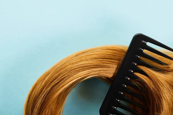 Vue du dessus du peigne en cheveux bruns sur fond bleu — Photo de stock