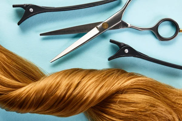 Draufsicht auf Klemmen und Scheren mit verdrehten braunen Haaren auf blauem Hintergrund — Stockfoto