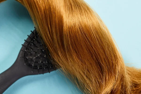 Top view of shiny brown hair and hairbrush on blue background — Stock Photo