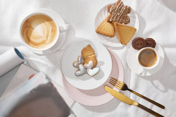 Vue du dessus des magazines, biscuits sucrés et café sur tissu blanc — Photo de stock