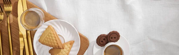 Top view of coffee with cookies and cutlery on cutting board on white cloth, panoramic shot — Stock Photo