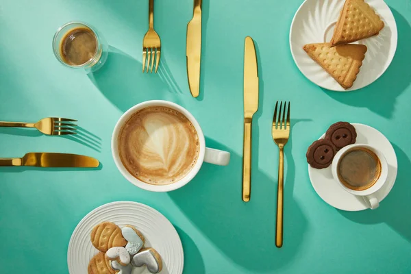 Vista dall'alto di gustosi biscotti e biscotti con caffè e posate dorate su superficie turchese — Foto stock