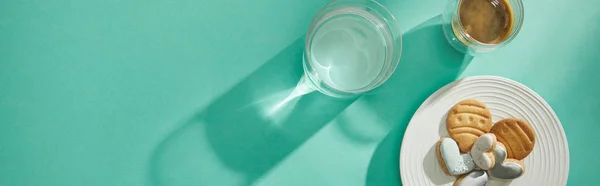 Top view of glass of water with coffee and tasty cookies on turquoise surface, panoramic shot — Stock Photo