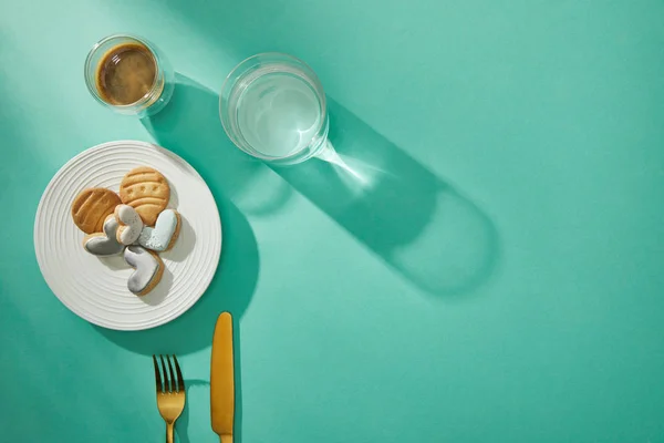 Top view of cookies with frosting, glass of water and coffee on turquoise background — Stock Photo