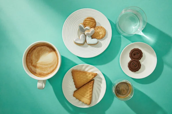 Top view of fresh cookies with coffee and glass of water on turquoise background — Stock Photo