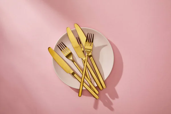 Top view of shiny golden cutlery on empty plate on pink background — Stock Photo