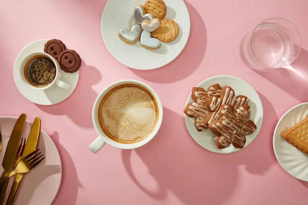 Top view of cups of coffee with fresh cookies and water on pink background — Stock Photo