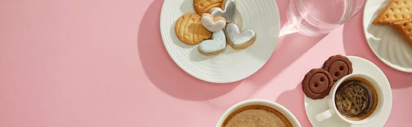 Vista superior de deliciosos biscoitos com xícaras de café e água na superfície rosa, tiro panorâmico — Fotografia de Stock