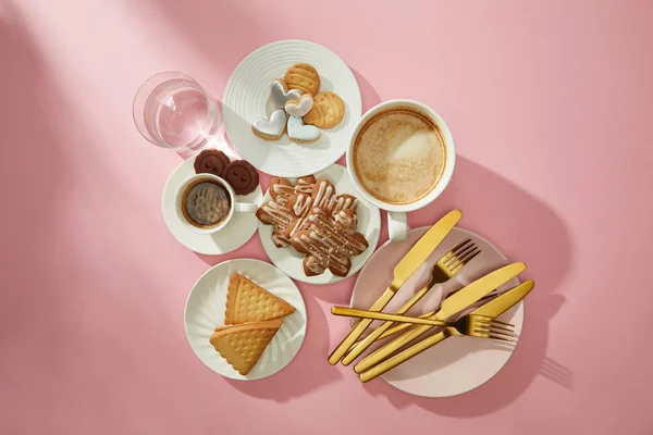 Draufsicht auf Kekse mit Glasur, Kaffee und Glas Wasser auf rosa Hintergrund — Stockfoto