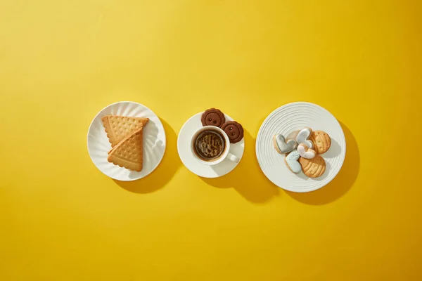 Top view of coffee cup with cookies on plates on yellow surface — Stock Photo