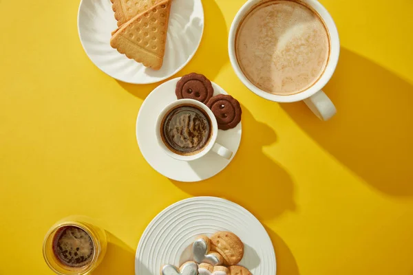 Vista superior de copos e copo de café fresco com biscoitos e biscoitos em fundo amarelo — Fotografia de Stock