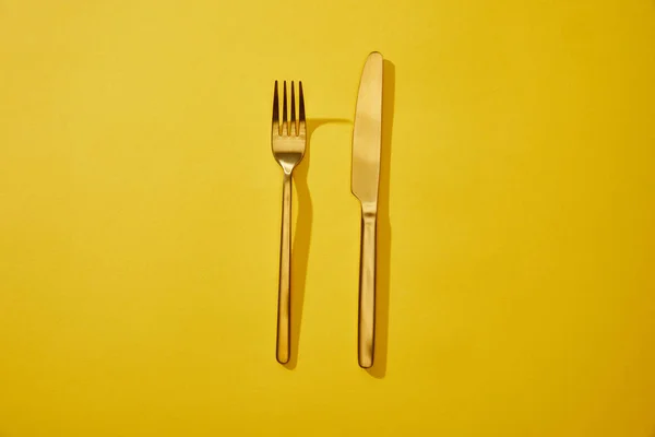 Top view of shiny fork and knife on yellow background with copy space — Stock Photo