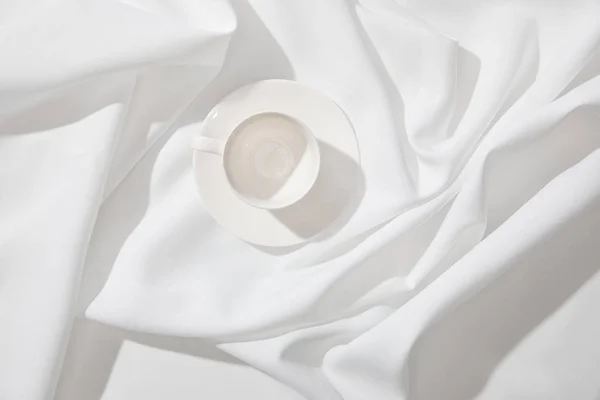 Верхний вид пустой чашки кофе с блюдцем на белой волнистой скатерти — стоковое фото
