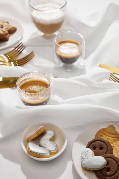 Selective focus of fresh coffee with delicious cookies on white wavy cloth — Stock Photo