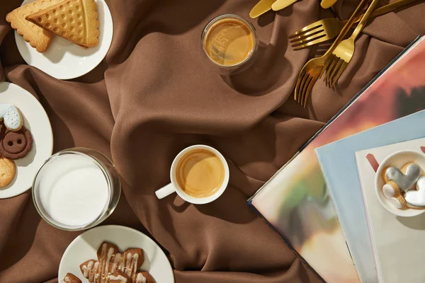 Ansicht von Zeitschriften mit frischen Keksen, Milch und Kaffee auf brauner Tischdecke — Stockfoto