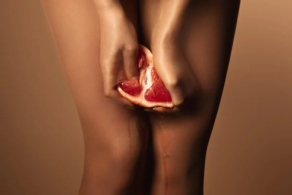 Abgeschnittene Ansicht einer Frau in Nylonstrumpfhosen, die Grapefruit halb isoliert auf braun drückt — Stockfoto