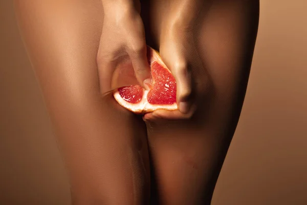 Abgeschnittene Ansicht einer Frau in Nylonstrumpfhosen, die Grapefruit halb isoliert auf braun drückt — Stockfoto