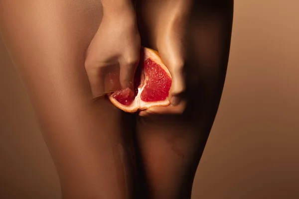 Cropped view of woman in nylon tights squeezing grapefruit half isolated on brown — Stock Photo