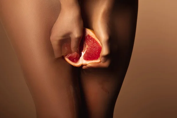 Vista cortada da mulher em meias de nylon espremendo toranja metade isolado em marrom — Fotografia de Stock