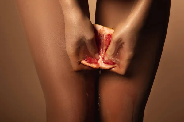 Обрізаний вид жінки в нейлонових колготках стискаючи грейпфрут наполовину ізольовані на коричневому — стокове фото
