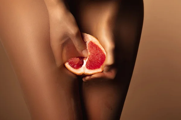 Vista cortada da mulher em meias de nylon espremendo toranja metade isolado em marrom — Fotografia de Stock