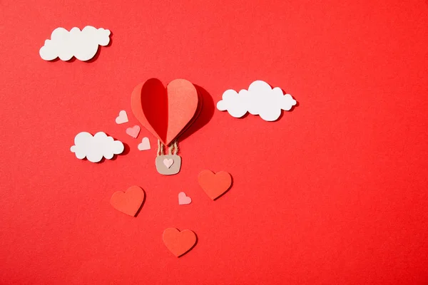 Vue du dessus du ballon d'air en forme de coeur en papier dans les nuages sur fond rouge — Photo de stock