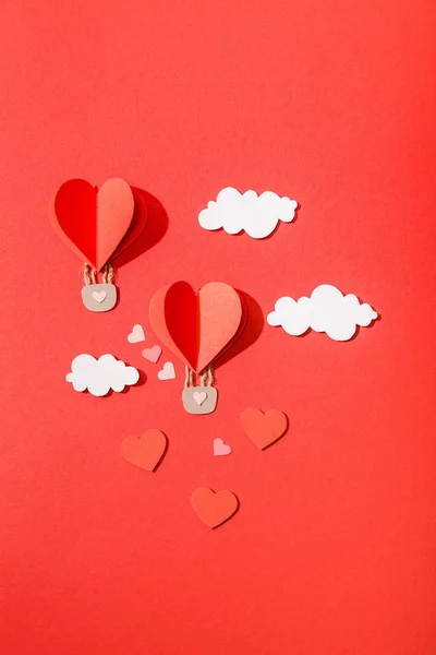 Vue du dessus des ballons à air en forme de coeur en papier dans les nuages sur fond rouge — Photo de stock