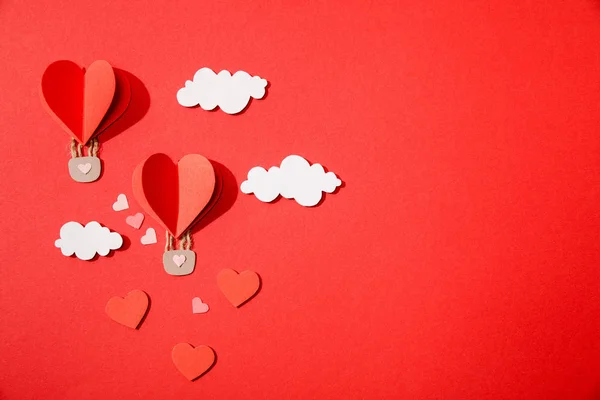 Top view of paper heart shaped air balloons in clouds on red background — Stock Photo