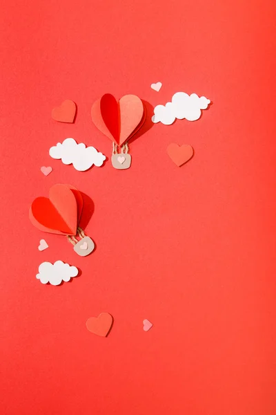 Top view of paper heart shaped air balloons in clouds on red background — Stock Photo