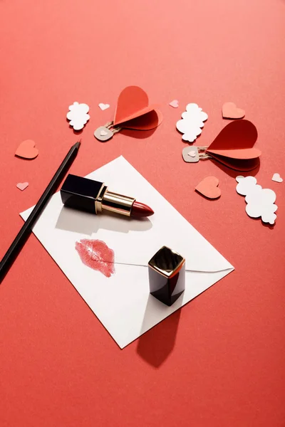 Paper clouds and heart shaped air balloons, envelope with lip print, lipstick and pencil on red background — Stock Photo