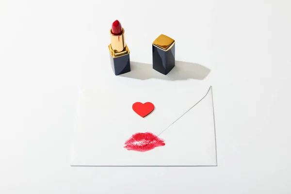 Briefumschlag mit Lippenprint und Herz in der Nähe von rotem Lippenstift auf weißem Hintergrund — Stockfoto