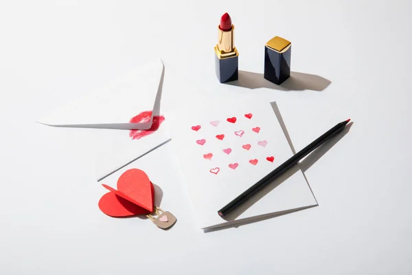Cartão de saudação com corações perto envelope com impressão labial, batom e lápis sobre fundo branco — Fotografia de Stock
