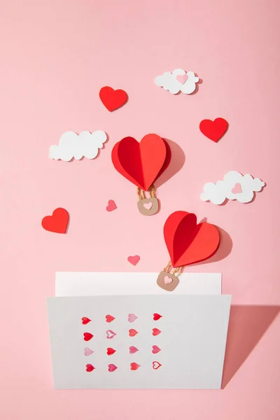 Top view of greeting card with hearts near paper heart shaped air balloons in clouds on pink — Stock Photo