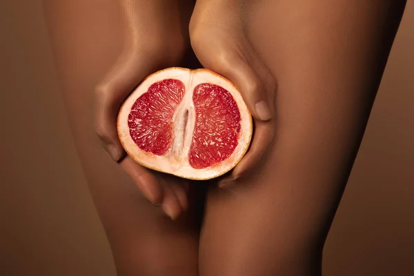 Vista cortada da mulher em meias de nylon segurando toranja metade isolado em marrom — Fotografia de Stock