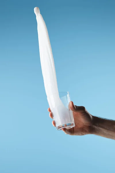 Cropped view of man holding glass with fresh white milk splash isolated on blue — Stock Photo