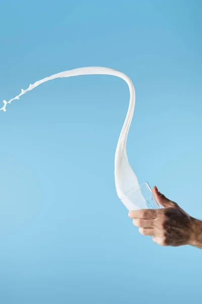 Cropped view of man holding glass with fresh white milk splash isolated on blue — Stock Photo