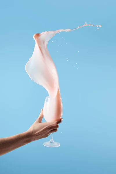 Vista recortada de la mujer sosteniendo vidrio con salpicadura de leche rosa fresca aislado en azul - foto de stock