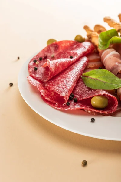 Vue rapprochée de délicieux plateau de viande servi avec des olives et des bâtonnets de pain sur fond beige — Photo de stock